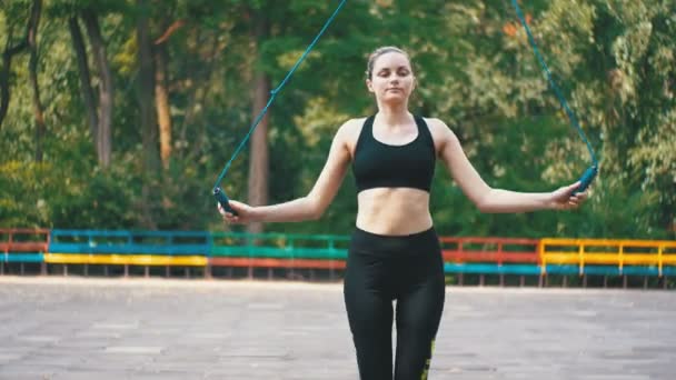 Mujer atleta joven en traje deportivo cómodo saltar la cuerda en un campo de deportes en el parque — Vídeo de stock