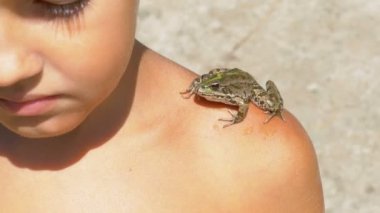 Nehri yakınında sahilde bir genç çocuğun omzuna oturan kurbağa