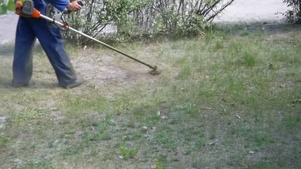 Homem corta grama usando um cortador de grama portátil — Vídeo de Stock