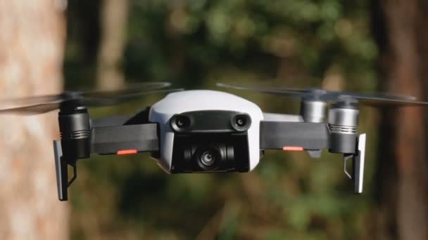 Lennokki kameran kanssa leijuu ilmassa. Quadcopter lentää maanpinnan yläpuolella metsässä — kuvapankkivideo