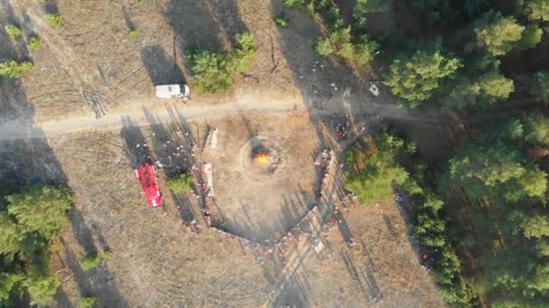 Flygfoto över organiserad insamling av folket nära en stor lägereld i en tallskog — Stockvideo