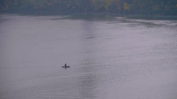 在一个阴天和寒冷的秋天, 一条小船上的人漂浮在河上。渔夫在池塘捕鱼 — 图库视频影像