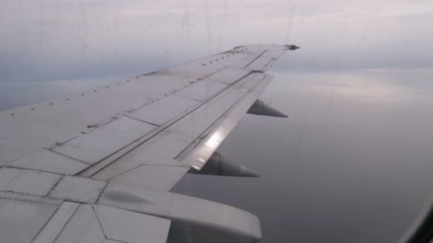 Вид из окна пассажирского самолета на крыло, летящее над облаками — стоковое видео