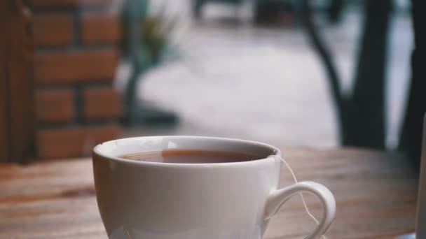 Белая чашка горячего чая на столе в кафе на фоне уличного окна — стоковое видео