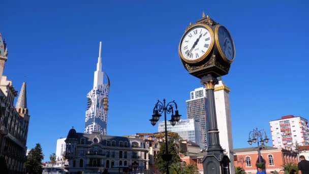 Reloj de calle en la Plaza de Europa en el fondo del rascacielos con la rueda de oro Ferris. Batumi, Georgia — Vídeo de stock