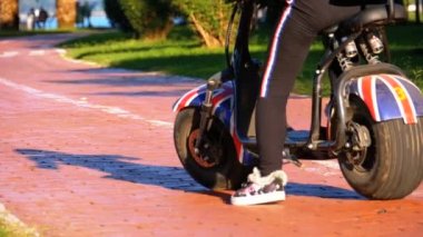 Kadın parkta bisiklet yolu üzerinde bir Elektrikli Scooter sürme. Ağır çekim