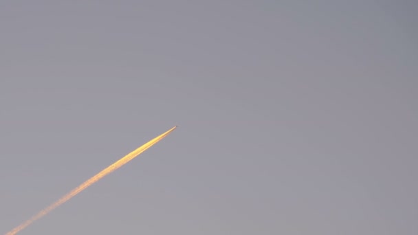 El avión de pasajeros vuela alto en el cielo y deja rastros de humo en la puesta del sol . — Vídeos de Stock