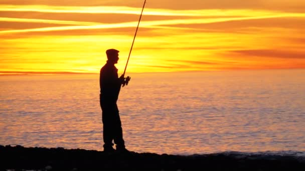 Silueta de un pescador con caña de pescar al atardecer sobre el mar — Vídeo de stock