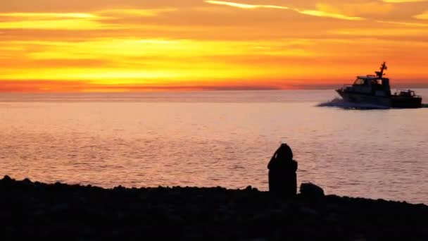Силуэт девушки, сидящей на пляже на закате и использующей смартфон — стоковое видео