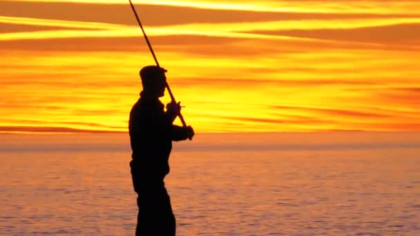 Silhuetten av en fiskare med ett fiskespö i solnedgången över havet — Stockvideo