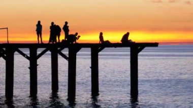 Gün batımında deniz iskelede gençlerin siluetleri
