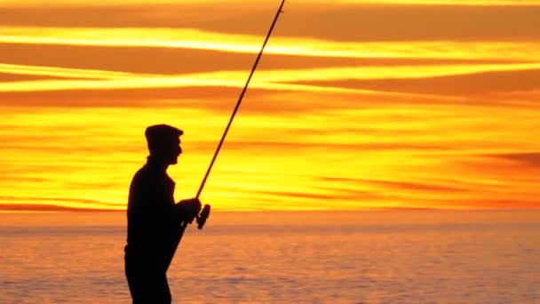 Silhouette d'un pêcheur avec une tige de pêche au coucher du soleil sur la mer — Video