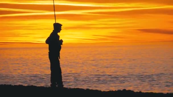 在海上空的日落时, 一名拿着钓鱼竿的渔民的剪影 — 图库视频影像