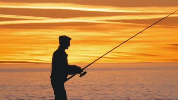 在海上空的日落时, 一名拿着钓鱼竿的渔民的剪影 — 图库视频影像