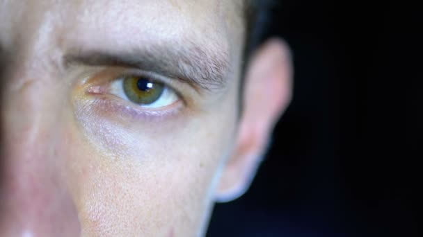 Крупним планом очі і обличчя молодого чоловіка, який працює за комп'ютером на чорному тлі — стокове відео