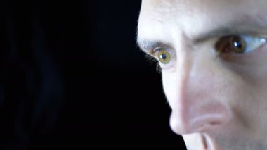 Siyah bir arka planda bilgisayarın başında çalışan genç bir adamın gözleri ve yüzü yakın plan.