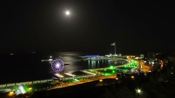 Top View of a Big City at Night, Ferris Wheel on the Background of the Sea and the Moon Path. Движение на дорогах. Время покажет — стоковое видео