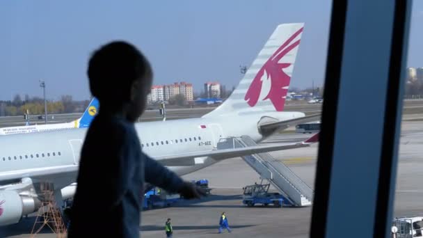 Silhouette eines kleinen Jungen vor dem Terminal-Fenster beim Blick auf die Flugzeuge — Stockvideo