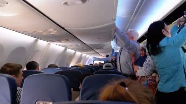 Посадка. Пассажиры воздушного судна с вещами проходят между креслами самолета в салоне на свои места . — стоковое видео