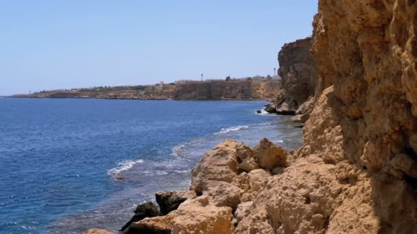 Rocky Beach en Egypte. Plage dans une baie sur la côte avec des vagues dans la mer bleue et les récifs coralliens. Mouvement lent 