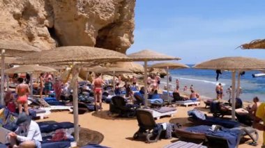 Mısır'da plaj. Kızıldeniz Sahili'ndeki tatil köyü. İnsanlar şemsiye ve şezlongile plajda rahatlayıp güneşlenmekte