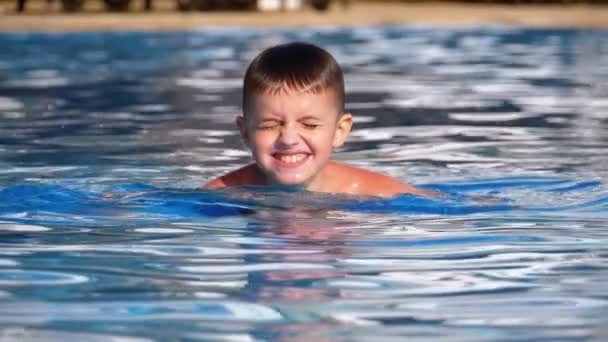 Niño feliz nada en una piscina con agua azul. Moción lenta — Vídeo de stock