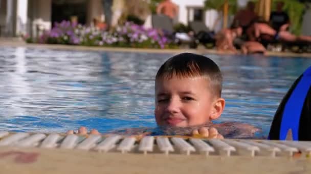 Счастливый мальчик с колясками плавает в бассейне с голубой водой. Slow Motion — стоковое видео