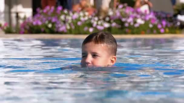 Счастливый мальчик плавает в бассейне с голубой водой в отеле. Slow Motion — стоковое видео