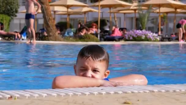 Счастливый ребенок плавает в бассейне с голубой водой в отеле. Slow Motion — стоковое видео