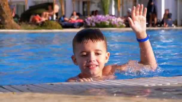Счастливый мальчик, играющий в бассейне с голубой водой — стоковое видео