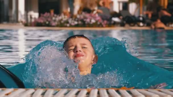 Menino feliz com chinelos Natação em uma piscina com água azul. Movimento lento — Vídeo de Stock