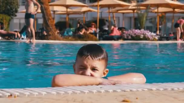 Счастливый ребенок плавает в бассейне с голубой водой в отеле. Slow Motion — стоковое видео