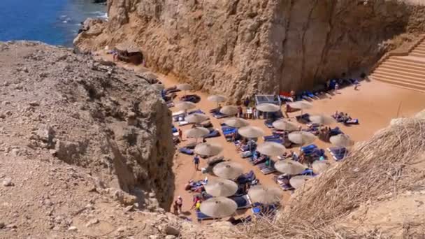 Felsstrand in einer Bucht mit Sonnenschirmen und Liegen in Ägypten am Roten Meer. — Stockvideo