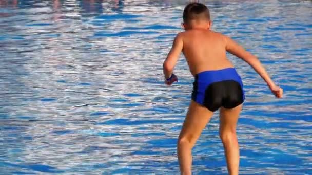 Glücklicher Junge, der in das blaue Wasserbecken springt. Zeitlupe — Stockvideo