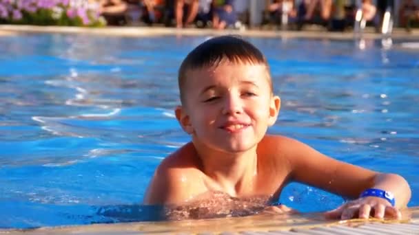 Šťastný chlapec hrající v bazénu s modrou vodou. Zpomaleně — Stock video