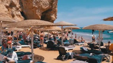 Mısır'da plaj. Kızıldeniz Sahili'ndeki tatil köyü. İnsanlar şemsiye ve şezlongile plajda rahatlayıp güneşlenmekte