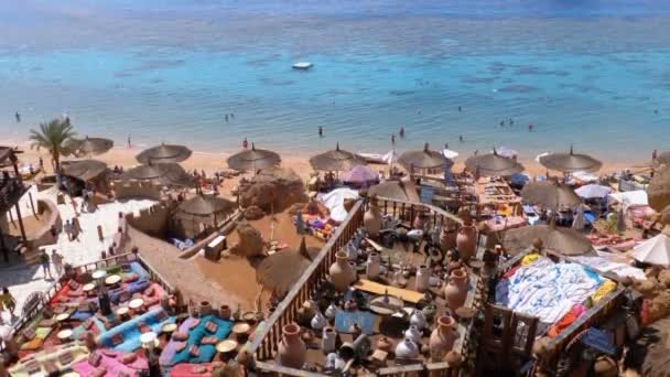 Playa rocosa con cafés árabes de estilo retro en la costa del Mar Rojo con sombrillas, camas de sol y corales. Egipto — Vídeo de stock
