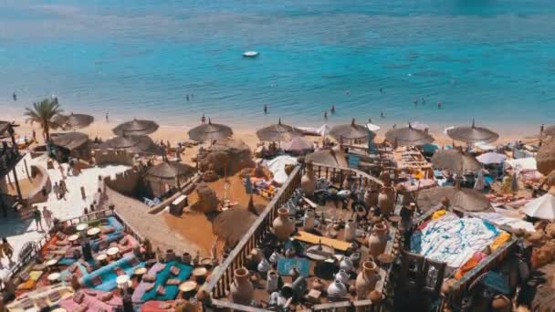 Playa rocosa con cafés árabes de estilo retro en la costa del Mar Rojo con sombrillas, camas de sol y corales. Egipto — Vídeo de stock