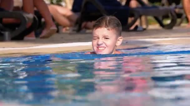 Happy Boy nada en una piscina con agua azul en el hotel. Moción lenta — Vídeo de stock