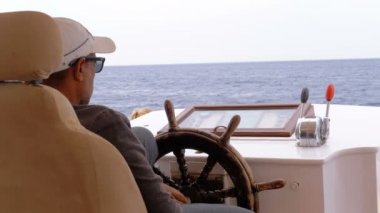 Bir zevk teknesinin direksiyonunda kaptan. Kaptan deniz yatı kontrol eder