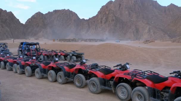 Группа красных квадроциклов стоит на парковке в пустыне на фоне гор. Водители квадроциклов — стоковое видео