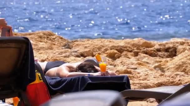 Gyönyörű lány feküdt egy naplopó a tengerparton egy koktél a pohár a kezében — Stock videók