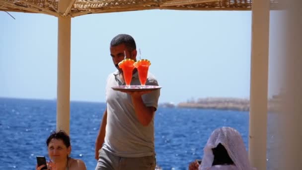 ビーチのウェイターは、エジプトのトレイにエキゾチックなフレッシュジュースやカクテルを運びます。スローモーション — ストック動画