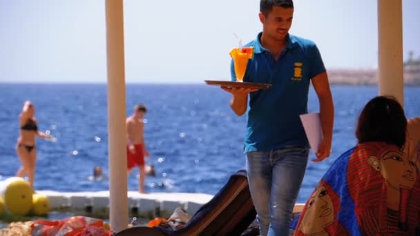 Camarero en la playa lleva exóticos jugos frescos y cócteles en una bandeja en Egipto. Movimiento lento — Vídeo de stock