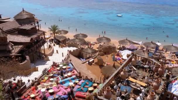 Playa rocosa con cafés árabes de estilo retro en la costa del Mar Rojo con sombrillas, camas de sol y corales. Egipto — Vídeos de Stock