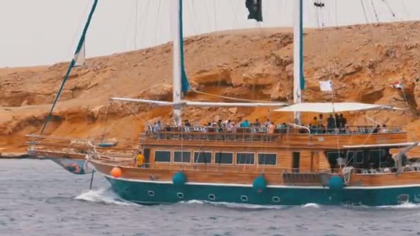 Mooie houten jacht met toeristen is zeilen in de stormachtige zee op de achtergrond van rotsen. Egypte — Stockvideo