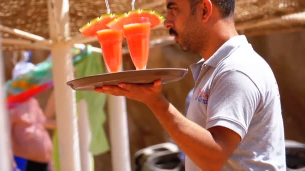 Der Kellner am Strand trägt exotische frische Säfte und Cocktails auf einem Tablett in Ägypten. Zeitlupe — Stockvideo