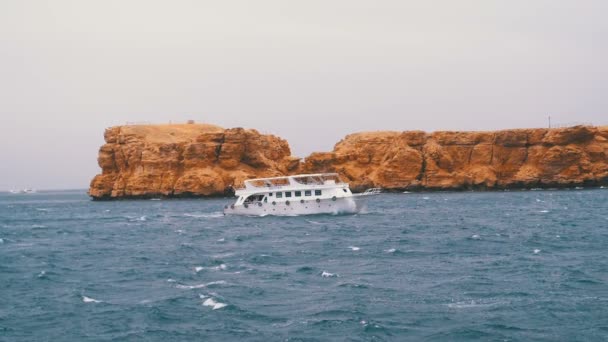 観光客と遊覧船は岩を背景に嵐の海で航海しています。エジプト — ストック動画