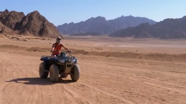 Flicka på en fyrhjuling rider genom öknen i Egypten på bakgrund av berg — Stockvideo