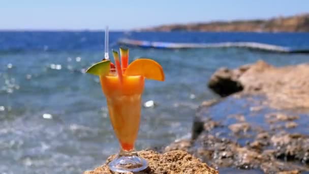 Tropisk färsk juice i ett glas med halm på stranden i Egypten står på en klippa vid havet — Stockvideo